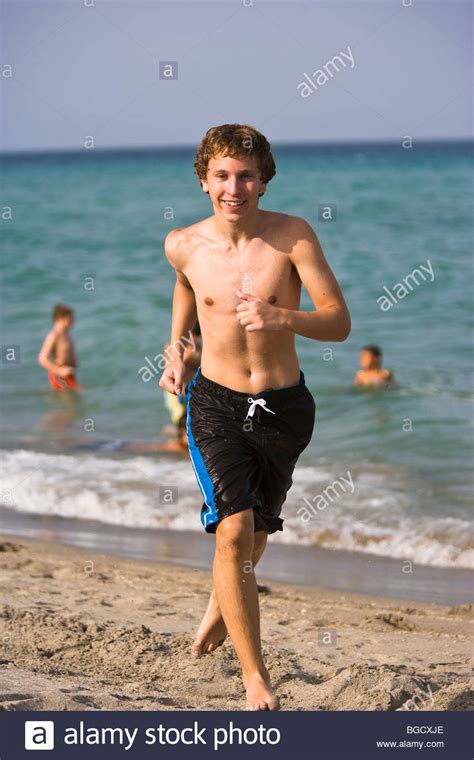 Teen boy running in swim trunks and on the beach, smiling ...