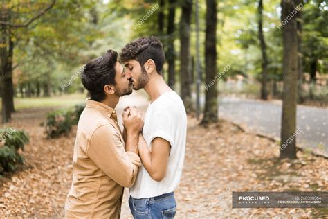 Young gay couple holding hands and kissing in autumnal park — lgbt ...